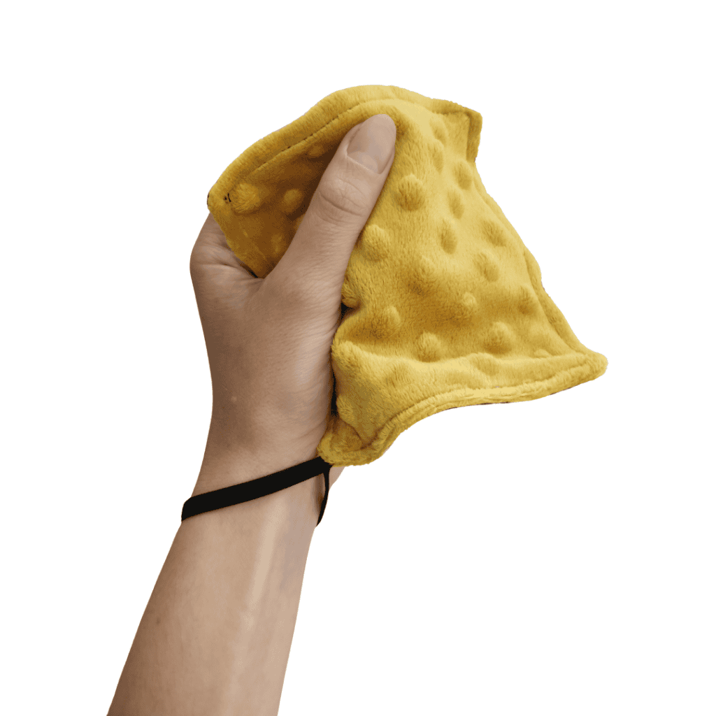 Atelier textures avec matériel sensoriel handicap moteur : Happy Senso, mousse et Mini SAM 4 Main tenant un carré sensoriel jaune en tissu à reliefs pour stimulation tactile